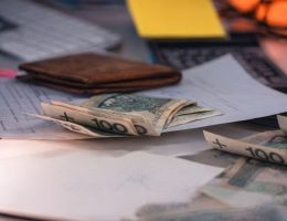 Sedlar, en plånbok och dokument på ett skrivbord som visar företagets kassaflöde.