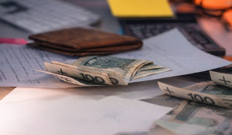 Sedlar, en plånbok och dokument på ett skrivbord som visar företagets kassaflöde.