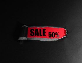 Svart papper med ett rivet hål som avslöjar texten SALE 50 procent på röd bakgrund.